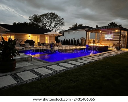 Magnificent glowing pool, cascading waterfall firepit and outdoor pavilion on a stormy summer night.  The weather does not detract from this luxurious backyard space and its modern design attributes