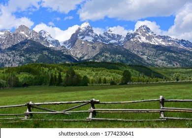the magnificent peaks of the grand teton mountain range with a split rail fence in a pasture on a sunny day in grand teton national park, wyoming