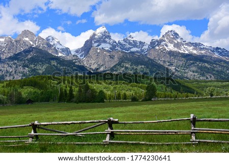 the magnificent peaks of the grand teton mountain range with a split rail fence in a pasture on a sunny day in grand teton national park, wyoming