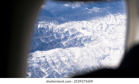 The magnificent scenery of endless snow-capped mountains seen from the window of the plane, the clear blue sky above, and the people playing with their mobile phones on the plane - Powered by Shutterstock