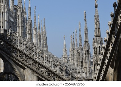 Magnificent spires and decorative details of Milan Cathedral (Duomo di Milano) rooftop, showcasing the beauty of Gothic architecture against a clear blue sky - Powered by Shutterstock