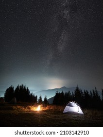 Magnificent View Of Night Starry Sky And Milky Way Over Grassy Hill With Illuminated Camp Tent And Campfire. Concept Of Hiking, Night Camping And Astronomy.