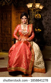 Magnificent young Indian bride in luxurious dress and precious jewelry is sitting in a chair in a luxury apartment. Classic vintage interior. Wedding fashion.