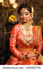 Magnificent young Indian bride in luxurious bridal costume with makeup and heavy jewellery is sitting in a chair in with classic vintage interior in studio lighting. Wedding fashion.