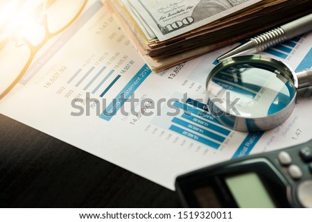 Magnifier glass calculator and financial data on businessman 's desk for analysis and find the best stock from stock market.