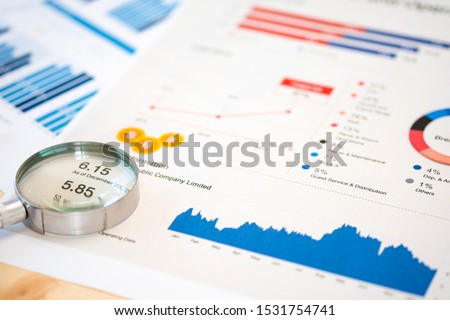 Magnifier glass and financial data on businessman 's desk for analysis and find the best stock from stock market.