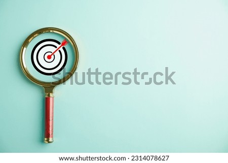 The magnifier glass highlights a target board, emphasizing the business objective, target search concept, and success. Isolated on a background with copy space.