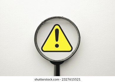 Magnify glass focus on Exclamation mark on a yellow sing or Warning sign over white background Attention sign,Exclamation mark,warning sign concept.