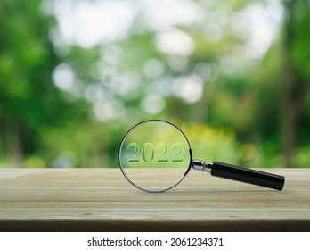 Magnifying Glass With 2022 Text And Financial Graph On Wooden Table Over Blur Green Tree In Garden, Business Happy New Year 2022 Research Concept