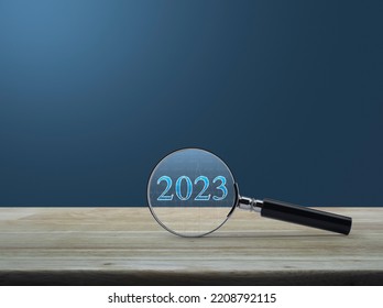 Magnifying Glass With 2023 Text And Financial Graph On Wooden Table Over Light Blue Wall, Business Happy New Year 2023 Research Concept