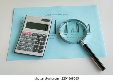 Magnifying Glass And Calculator On Top Of Sales Revenue Report With Charts. Business Performance Concept.