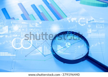 Magnifying glass and documents with analytics data lying on table,selective focus