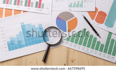 Magnifying glass and documents with analytics data lying on wood table