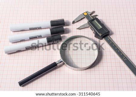 Magnifying glass, electronic slide calipers and pens on a graph paper