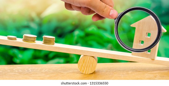 A magnifying glass explores a stack of coins on scales and a wooden house. Rent monthly payment. Real estate concept. Deopozit interest rates, mortgage interest. Affordable housing. Selective focus