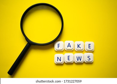Magnifying glass with "fake news" message made with letter game blocks, over a bright yellow background. Conceptual image of the importance of recognizing fake news.
