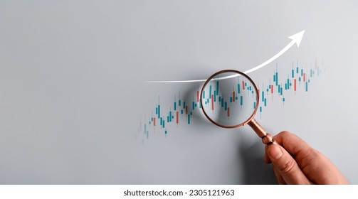 Magnifying glass focus on technical graph analyzing stock market profit trend. Businessman hand holding magnifier and zooming rising bar chart. Business economy and financial growth concept. - Powered by Shutterstock