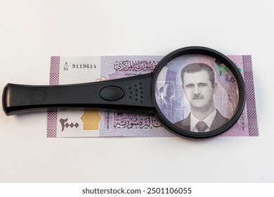 Magnifying glass focused on President Bashar Al Assad, portrait from syrian 2000 banknote isolated on white background