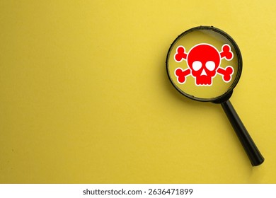 Magnifying glass focusing on a red skull and crossbones symbol. Concept of investigating danger,warning signs,hazard identification, risk assessment,identifying threats,or toxicity.Yellow background.
