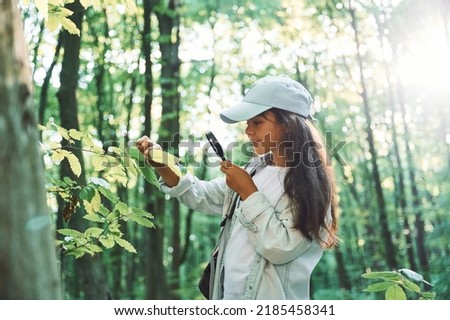 With magnifying glass. Girl is in the forest at summer day time discovering new places.