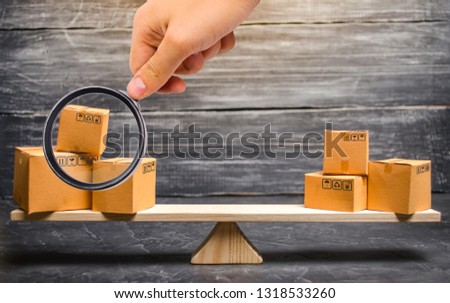 Magnifying glass is looking at the piles of boxes on the scales. Trade balance and calculation by barter. import and export of goods. Trade balance. Goods turnover between two subjects or countries.
