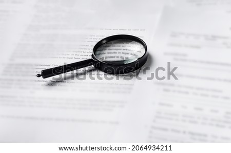 Magnifying glass lying over heap of paper documents. Investigation and financial audit concept.