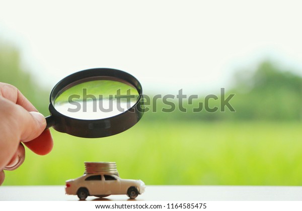 Magnifying Glass with miniature car searching\
for rent car on green\
background.