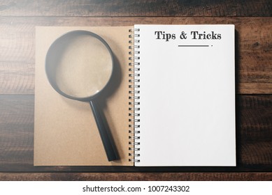 Magnifying Glass And Notebook With TIPS AND TRICKS Word With Copy Space On Wooden Table. Tips And Tricks Concept