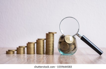A magnifying glass on a coin in a glass jar. Coin ladder from low to high. Business concepts, investments and risks.The concept of finding investment sources and fund sponsors Find available loans.