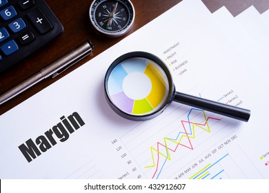 Magnifying glass on colourful pie chart with "Margin" text on paper, dice, spectacles, pen, laptop calculator on wooden table - business, banking, finance and investment concept - Shutterstock ID 432912607