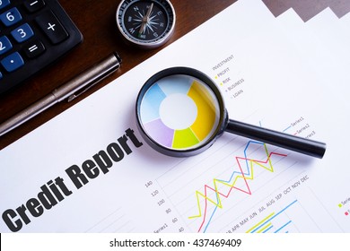 Magnifying glass on colourful pie chart with "Credit report" text on paper, dice, spectacles, pen, laptop calculator on wooden table - business, banking, finance and investment concept
