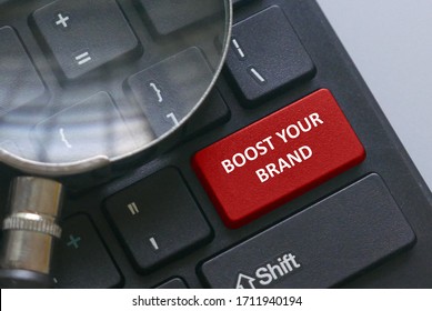 Magnifying glass on a computer keyboard with red button written with advice Boost your brand.