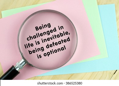 Magnifying glass on papers with word quote of "Being challenged in life is inevitable,being defeated is optional" written on it.