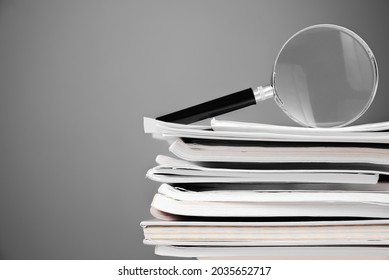 Magnifying glass on the pile of documents and textbooks, searching information concept