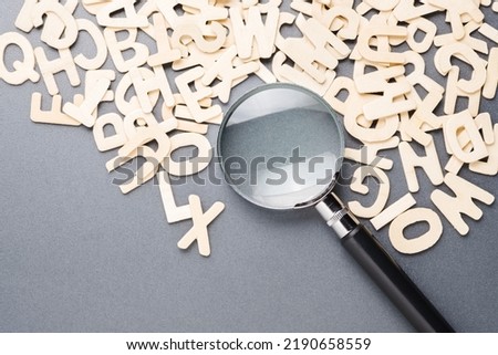 Magnifying glass on the pile of wooden English alphabets, glossary, and keyword, search the right word for communication, learning English concept