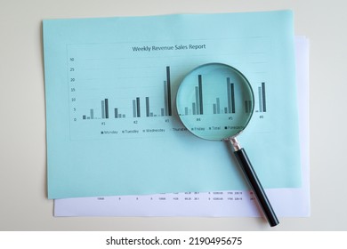 Magnifying Glass On Top Of Sales Revenue Report With Charts. Top View. Business Performance Concept.