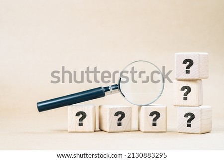 Magnifying glass on wood cubes with many question marks, confusing, frequently asked questions, and doing test concept