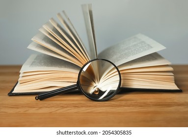 Magnifying glass and open books with turning pages on wood table. Reading and studying concept. - Shutterstock ID 2054305835