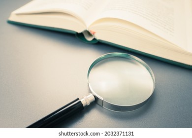 Magnifying glass and opened book on the desk, learning, research or searching information concept