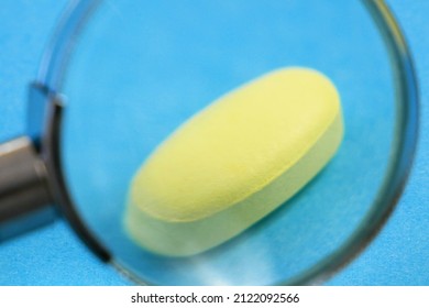 magnifying glass and pill on blue background. checking ingredients and effectiveness of medicine. fake pills concept,  closeup