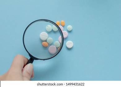 Magnifying glass with pills on blue background. pharmaceutical inspection identifies pills. Medicinal substance quality concept.