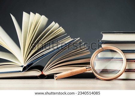 Magnifying glass rest on the book pile on the table, research information, glossary, education concept