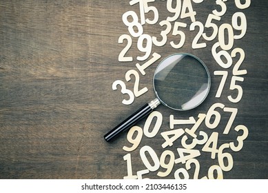 Magnifying glass in scattered numbers on wood background, calculation, mathematics concept - Shutterstock ID 2103446135