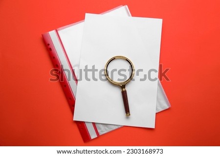 Magnifying glass, sheet of paper and folder on red background, top view