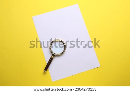 Magnifying glass and sheet of paper on yellow background, top view