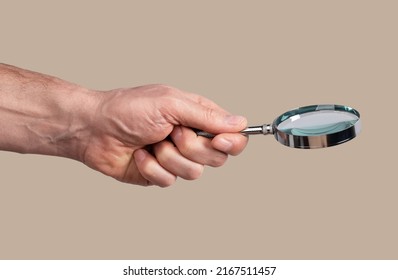 Magnifying glass side view in male hand close up over beige background. High quality photo