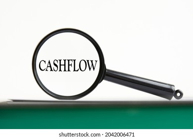 Magnifying Glass With Text Cashflow On Notebook With Green Pages, White Background