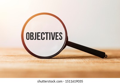 Magnifying glass with text Objectives on wooden table.