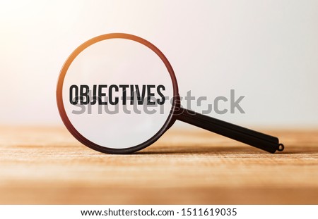 Magnifying glass with text Objectives on wooden table.