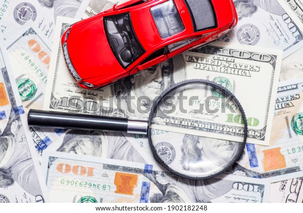 Magnifying glass and toy red car on dollar bills\
background. Saving money for car. Concept for advertising loan,\
collateral, pawnshop, car\
rental.